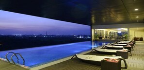 An infinity pool with lounge chairs and a view of the city at dusk. - Sayaji Raipur (Raipur)