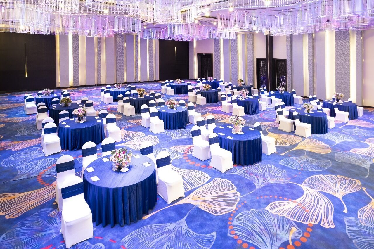 Un gran salón de baile con mesas redondas cubiertas con manteles azules y sillas blancas, dispuestas en filas.