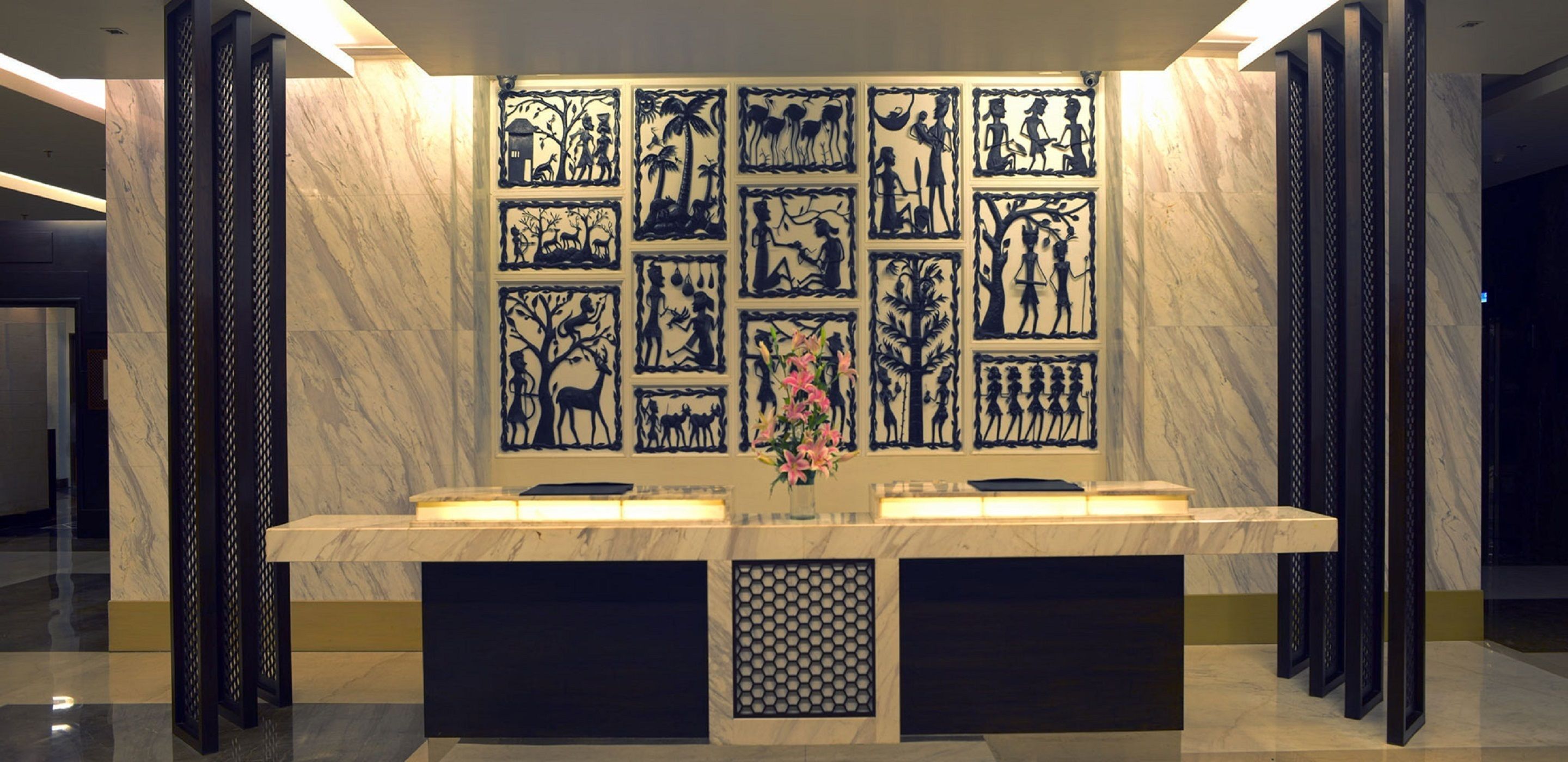 A reception desk with a marble countertop, a vase with flowers, and a wall with black silhouettes of various scenes.