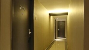 Ein Hotelgang mit einer dunklen Tür, auf der die Nummer „9204“ steht, und einem glänzenden, spiegelnden Boden.