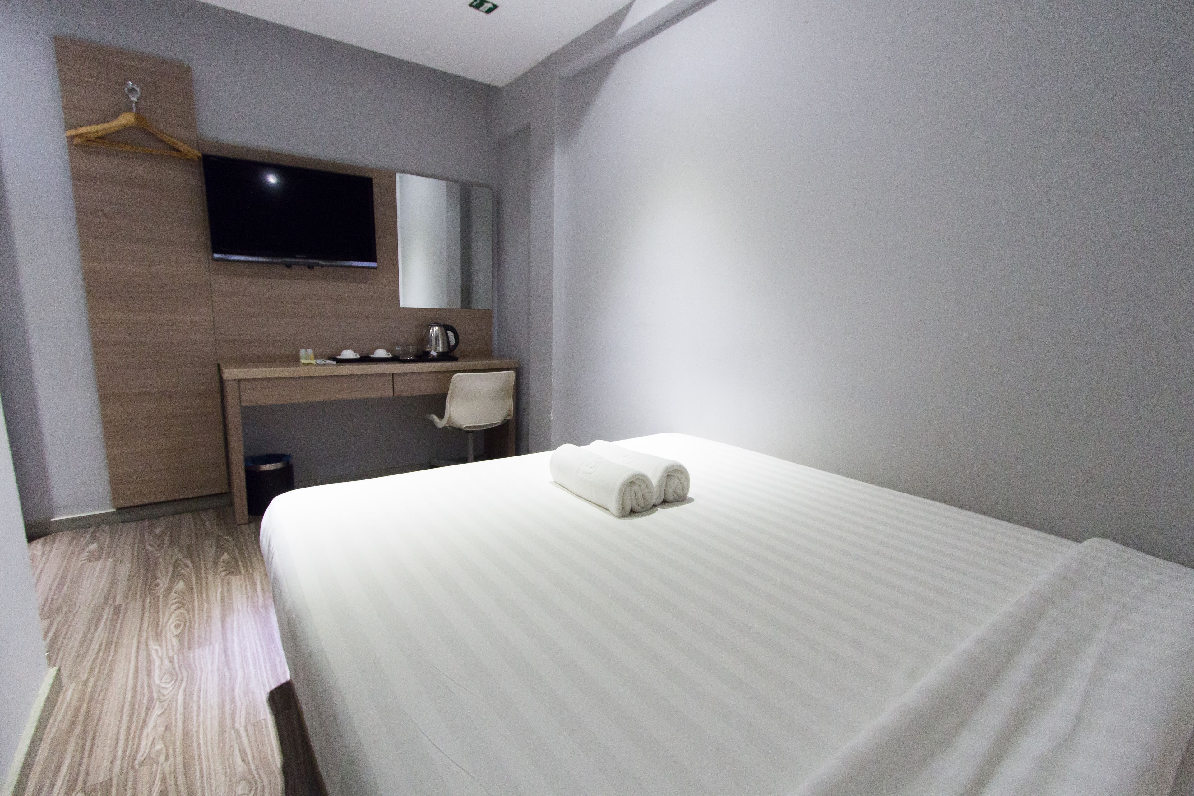 A hotel room with a bed, a desk, a chair, a television, and a mirror.