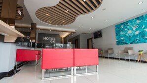 Eine moderne Hotelhalle mit einer Rezeption, einem roten Sitzbereich und einem großen, abstrakten Wandbild.