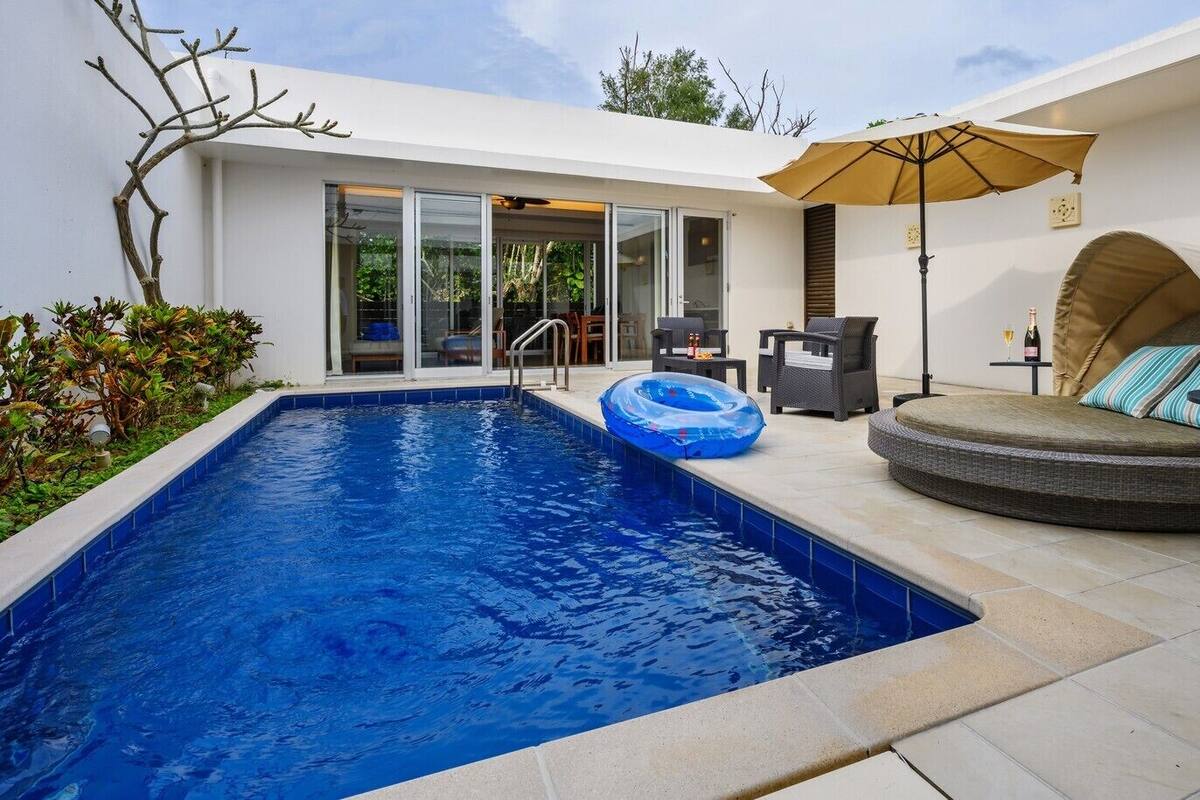 A swimming pool with a lounge area, including a covered seating area and a table with drinks.