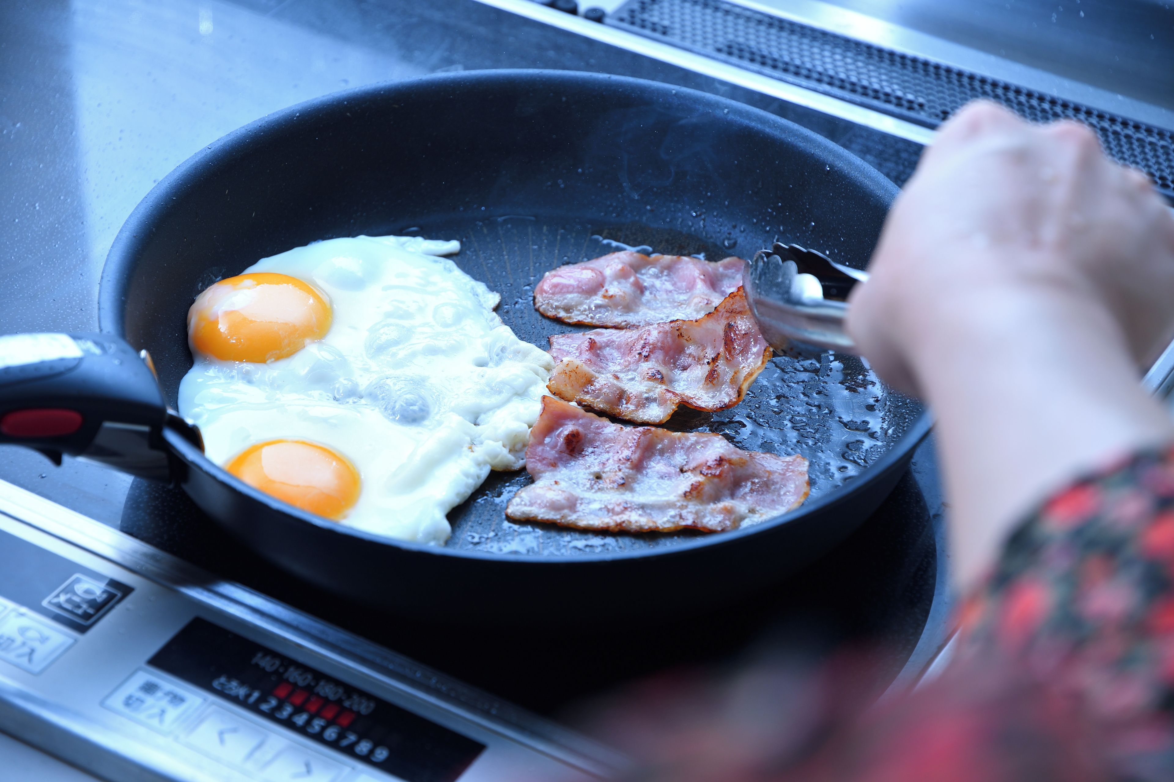 A frying pan with eggs and bacon on a stove.