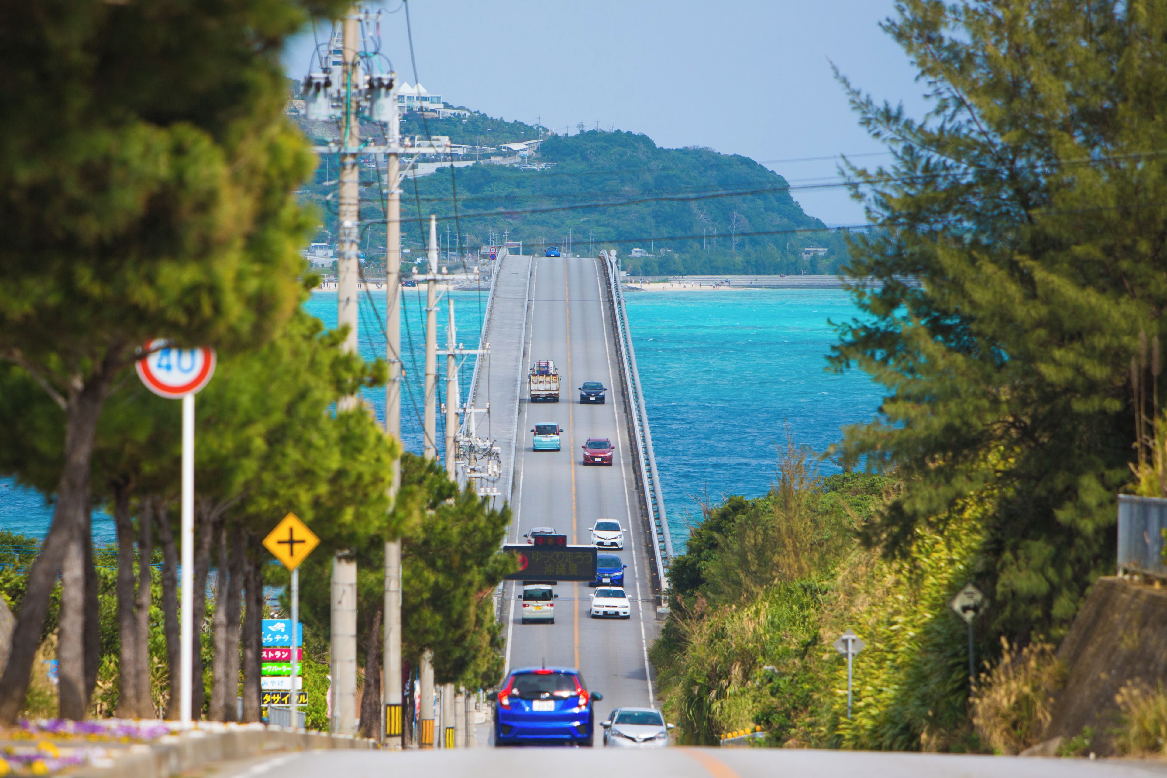 Una strada costiera con veicoli, un ponte e una spiaggia in lontananza.