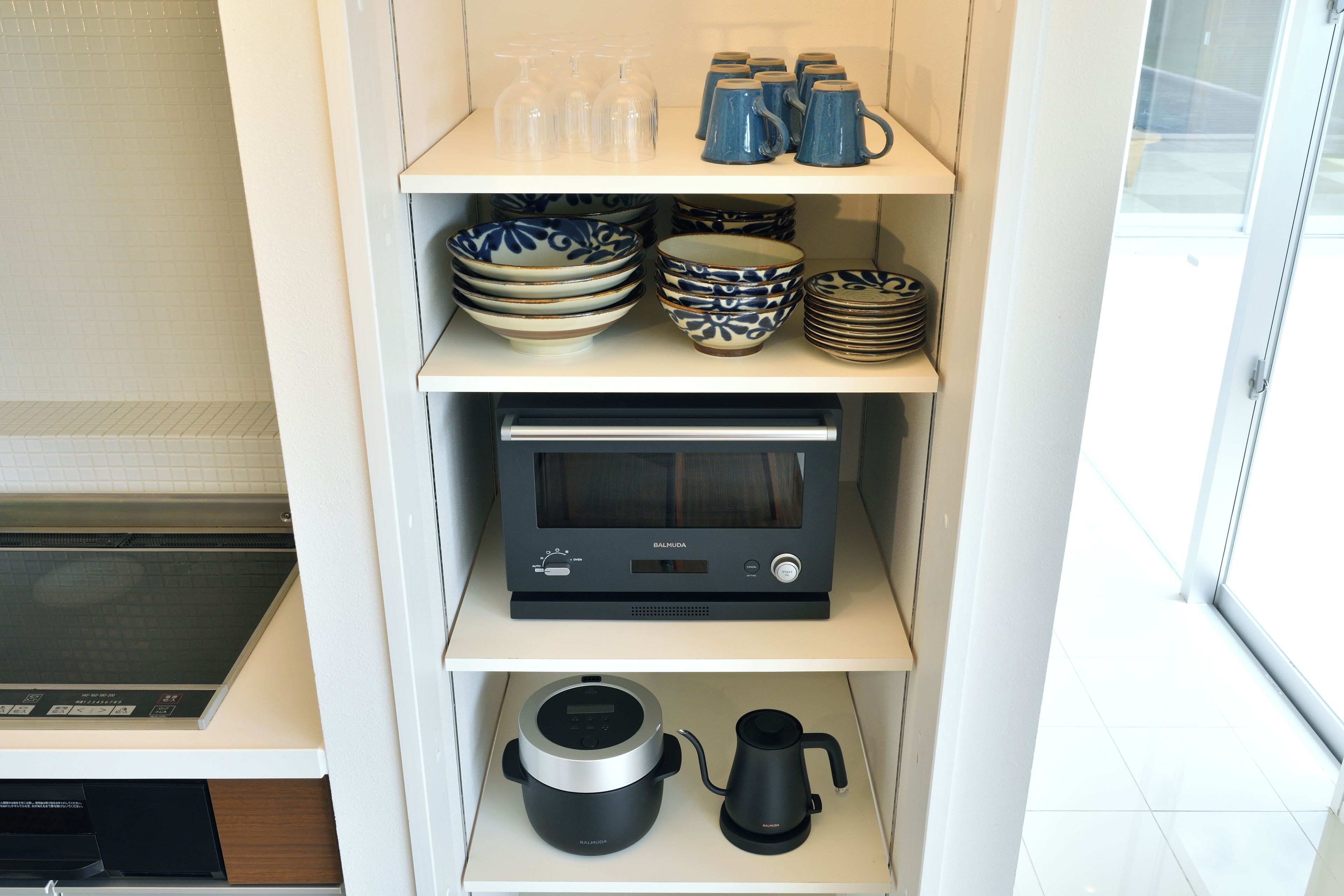 A kitchen with a microwave, a kettle, and a shelf with bowls and cups.
