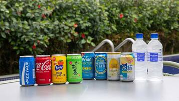 A variety of beverage cans and bottles arranged on a table outdoors with a hedge in the background.