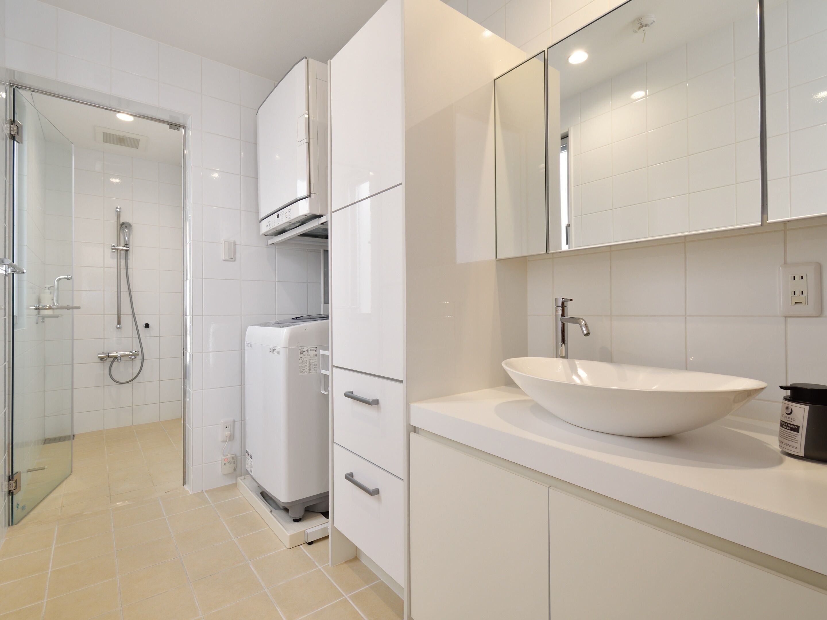 A modern bathroom with a glass-enclosed shower, a built-in washing machine, and a large white sink.