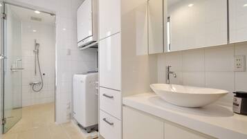 A modern bathroom with a glass-enclosed shower, a built-in washing machine, and a large white sink.