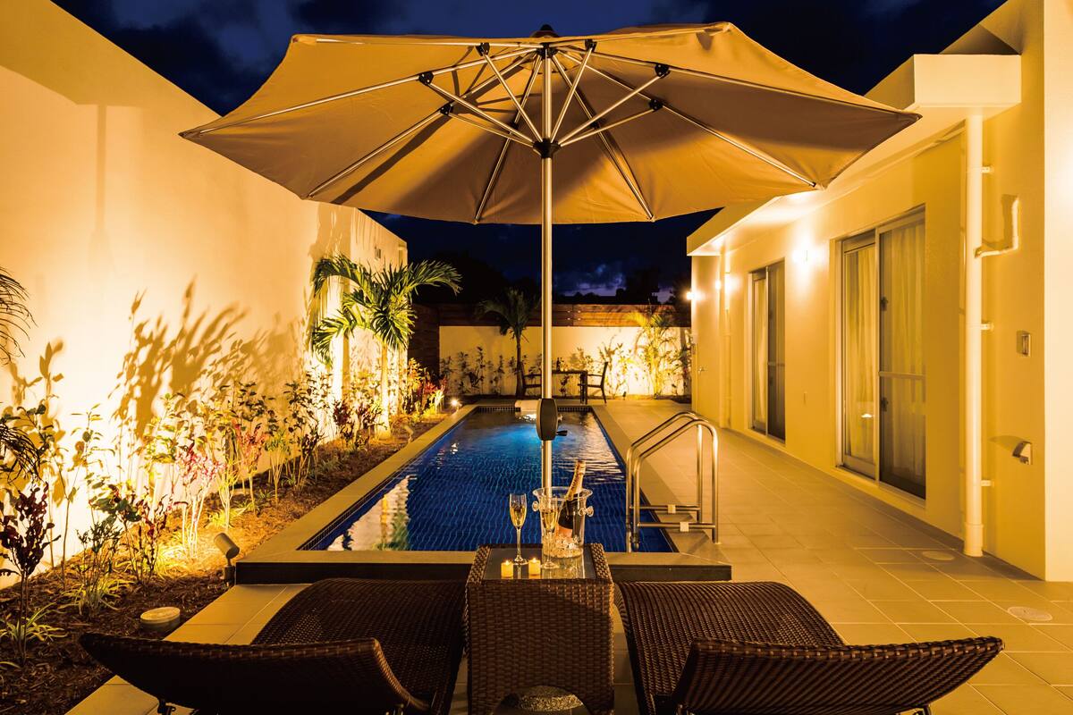 A poolside area with a hot tub, lounge chairs, and a large umbrella.