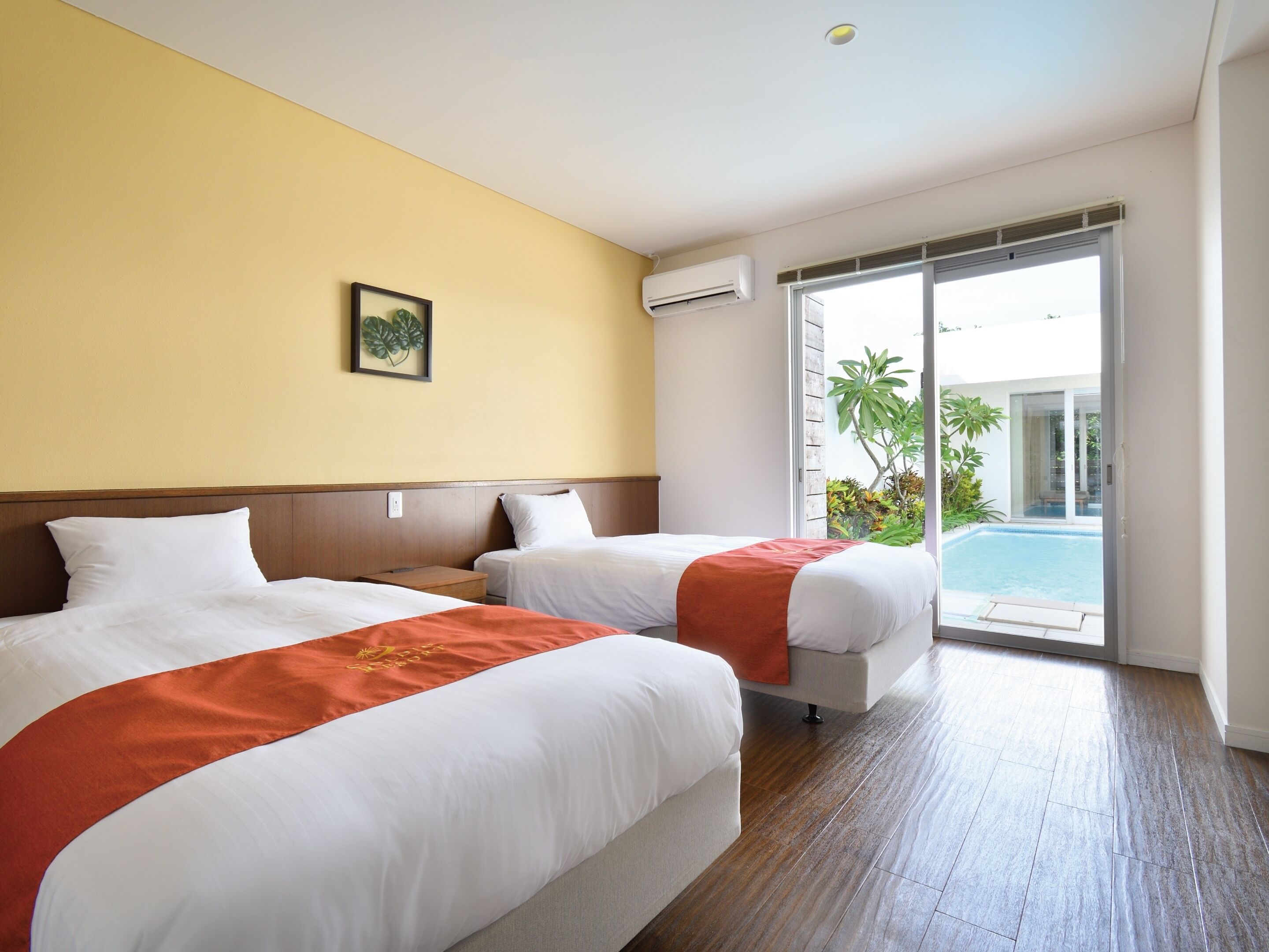 A hotel room with two beds, a wooden headboard, a framed picture on the wall, an air conditioning unit, and a view of a swimming pool through a glass door.