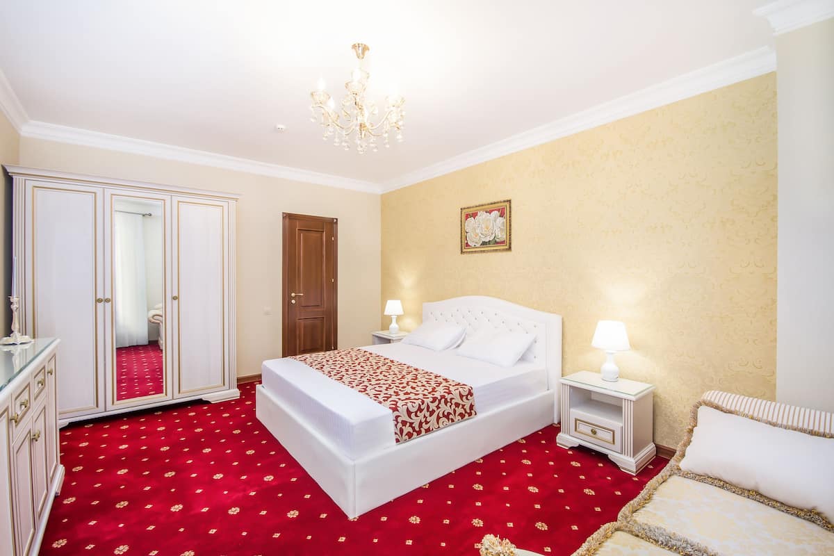 A hotel room with a large bed, a wardrobe, a nightstand with a lamp, and a red carpet.