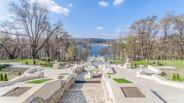 A park with a fountain, pathways, and a lake in the background. - Park Lane Hotel (Chisinau)