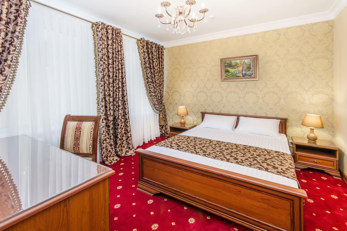 A hotel room with a wooden bed, a desk, and a chair. There are two bedside tables with lamps.