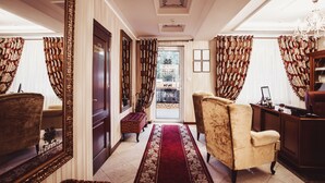 A hallway with a red carpet, a bench, a chair, and a desk with a chair. - Park Lane Hotel (Chisinau)