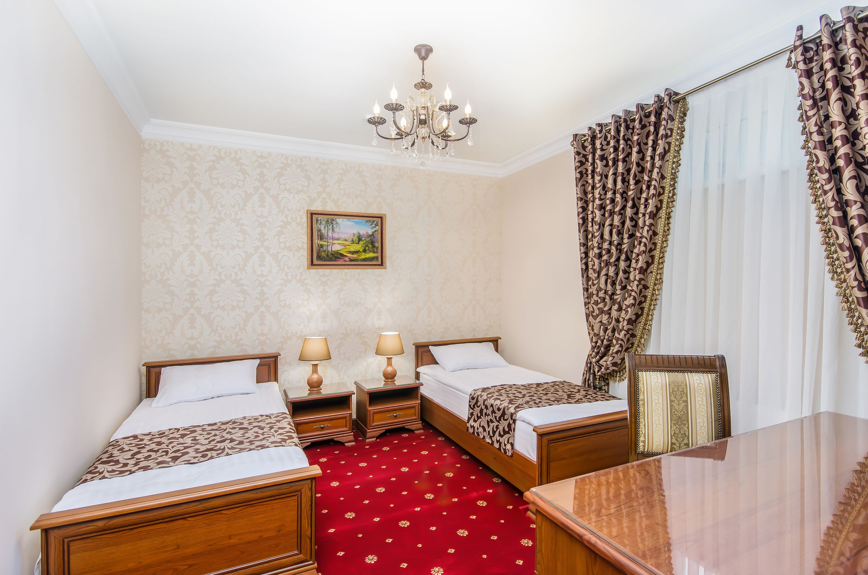 A hotel room with two beds, a wooden desk, a chandelier, and a red carpet.