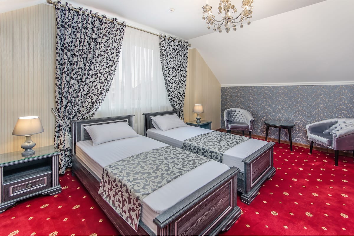 A hotel room with two beds, a chandelier, a red carpet, and a patterned wall.
