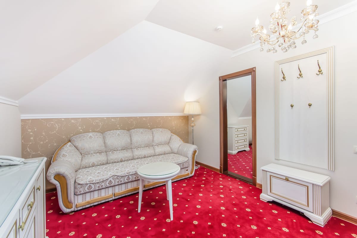 A room with a patterned sofa, a small round table, a mirror, a wardrobe, and a red carpet.