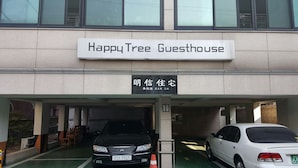 A building with a sign reading "Happy Tree Guesthouse" and another sign in a different language. There are two cars parked in front. - Happy Tree Guesthouse - Hostel (Seoul)