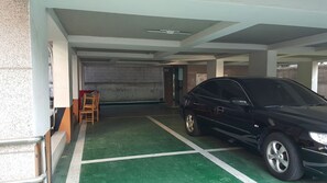 A parking garage with a green floor, a black car parked, and a chair near the wall.