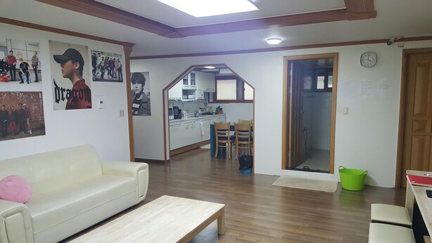 A living room with a sofa, a coffee table, and a dining area with chairs and a table. There is a kitchen visible through an archway. - Happy Tree Guesthouse - Hostel (Seoul)