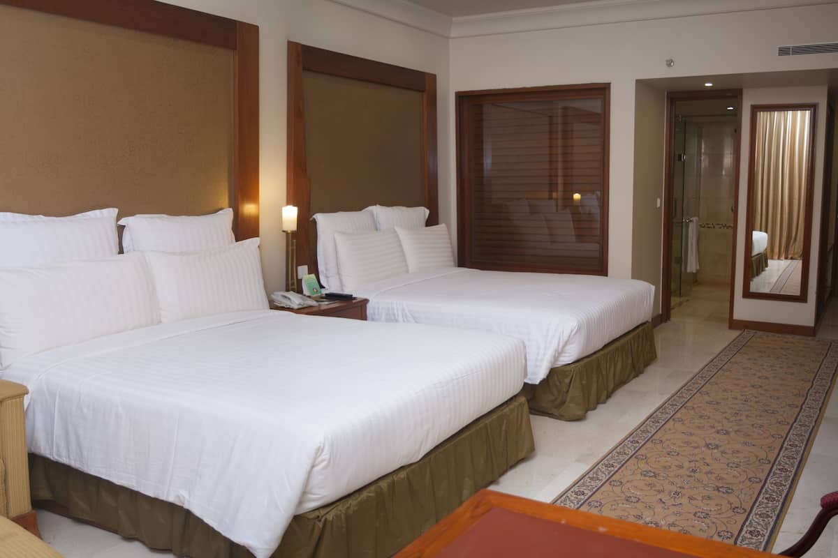 A hotel room with two beds, a nightstand, a lamp, and a mirror.