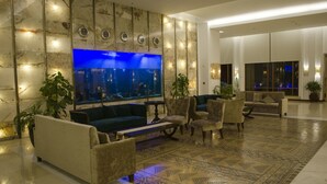 Een moderne lobby met een groot aquarium, comfortabele zithoeken en een vloer met een patroon.