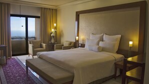 Een hotelkamer met een groot bed, een zithoek met stoelen, een kleine tafel met een bloevas en uitzicht door een groot raam.