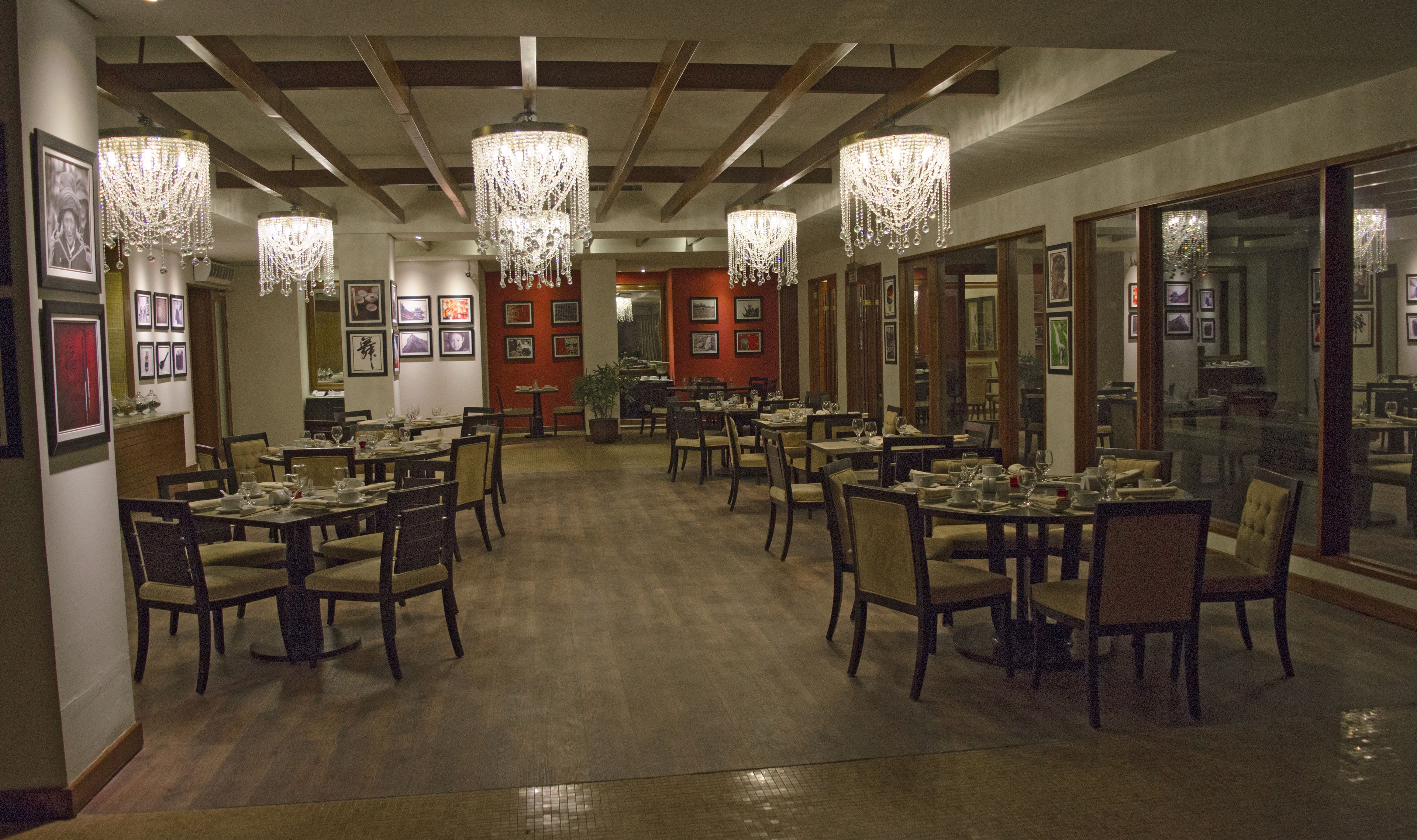 A restaurant with wooden tables and chairs, chandeliers, and framed pictures on the walls.