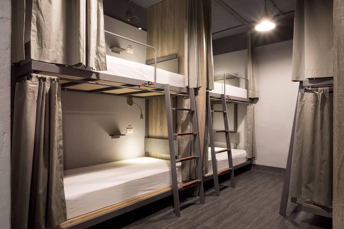 A bunk bed room with wooden floors, metal ladders, and beige curtains.