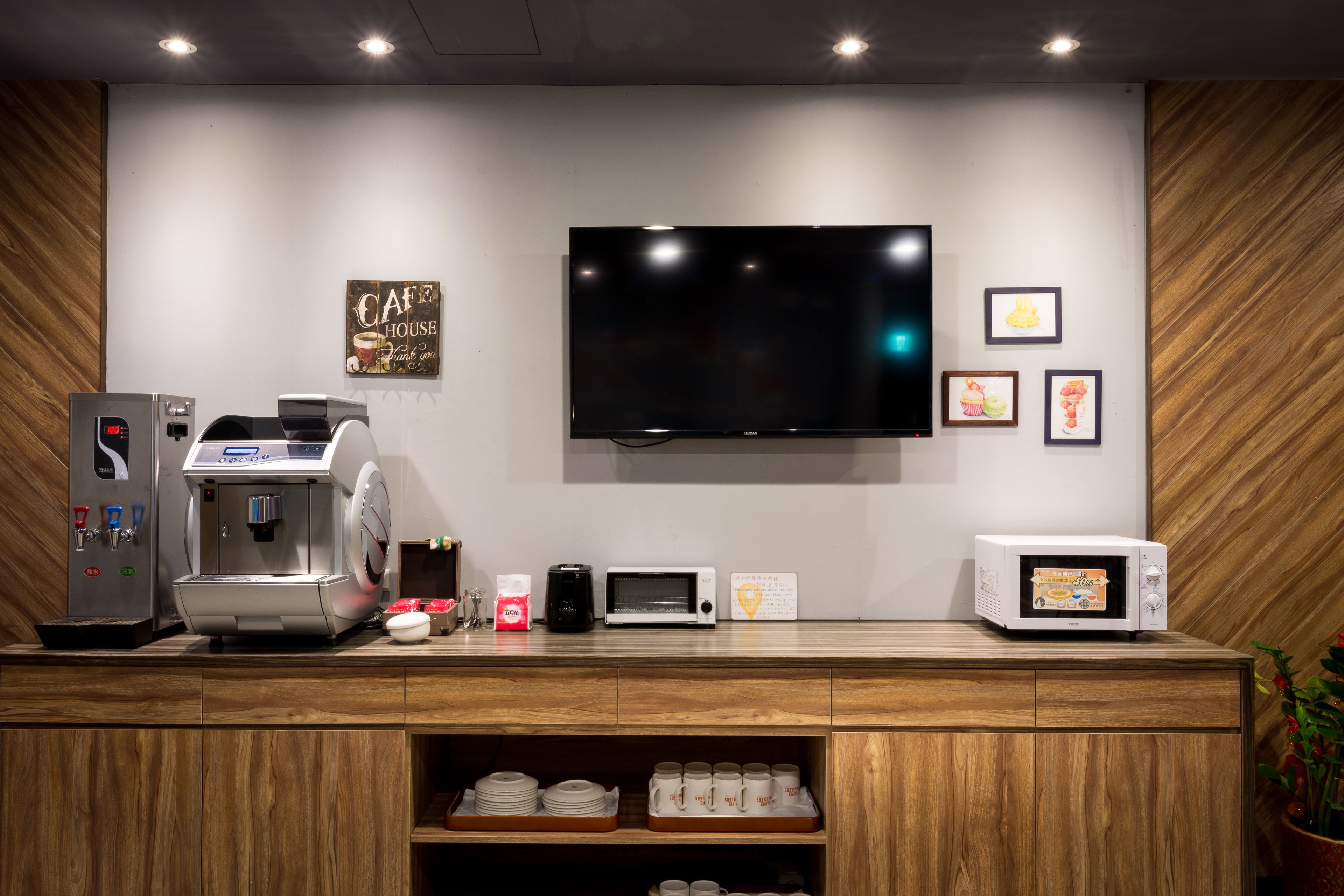 A coffee station with a coffee machine, a microwave, and a TV mounted on the wall.