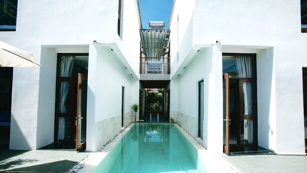 A modern building with a central swimming pool, white walls, and a covered walkway. - Green World Hoi An Villa (Da Nang)