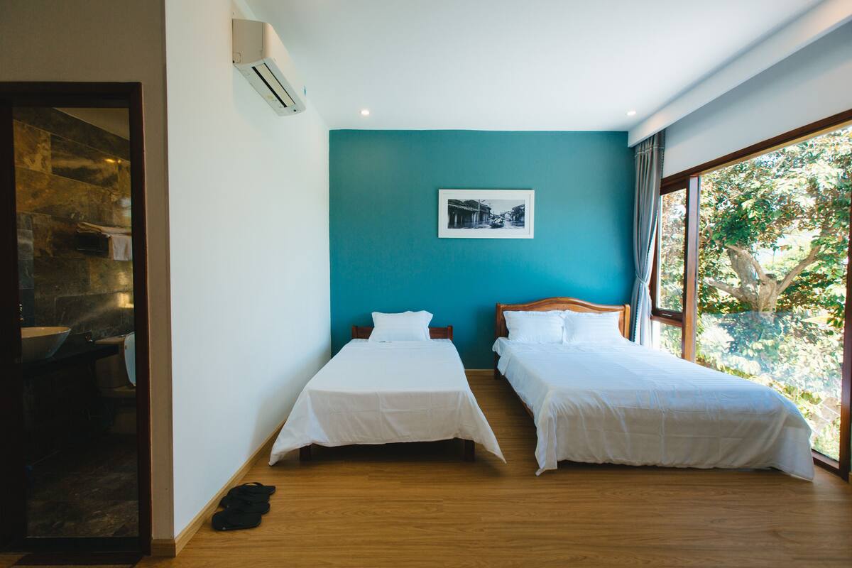 Une chambre avec deux lits, une salle de bain et une grande fenêtre donnant sur la forêt.