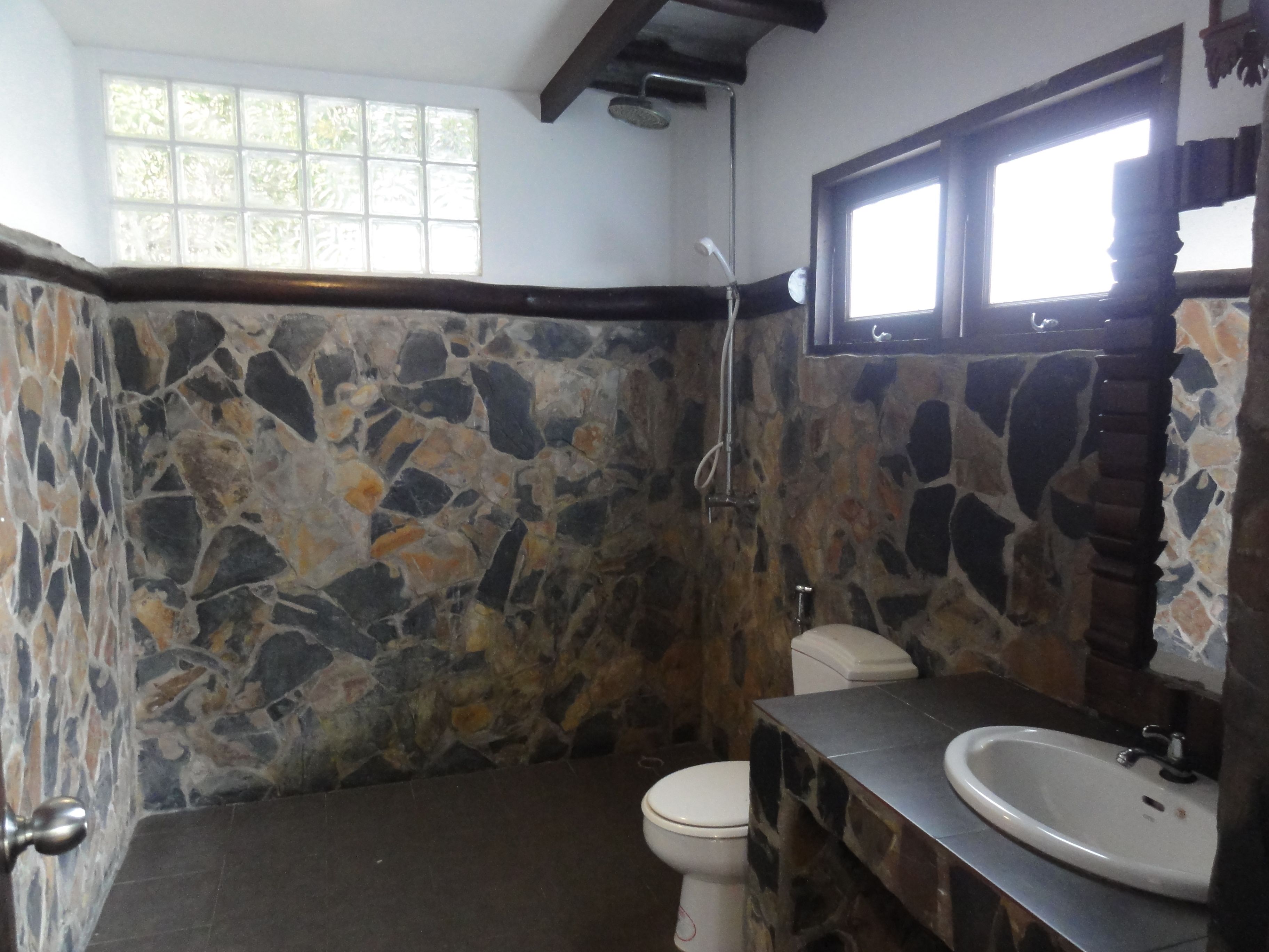 Un baño con pared de piedra, inodoro, lavamanos y ducha.