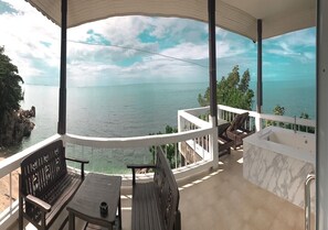 A balcony with a view of the sea, a seating area with a table and chairs, and a marble bathtub. - High Life Bungalow (Ko Pha-ngan)