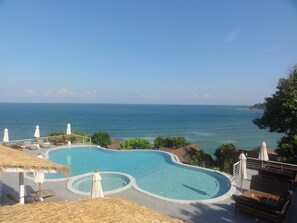 A pool area with a view of the ocean, lounge chairs, and umbrellas. - High Life Bungalow (Ko Pha-ngan)