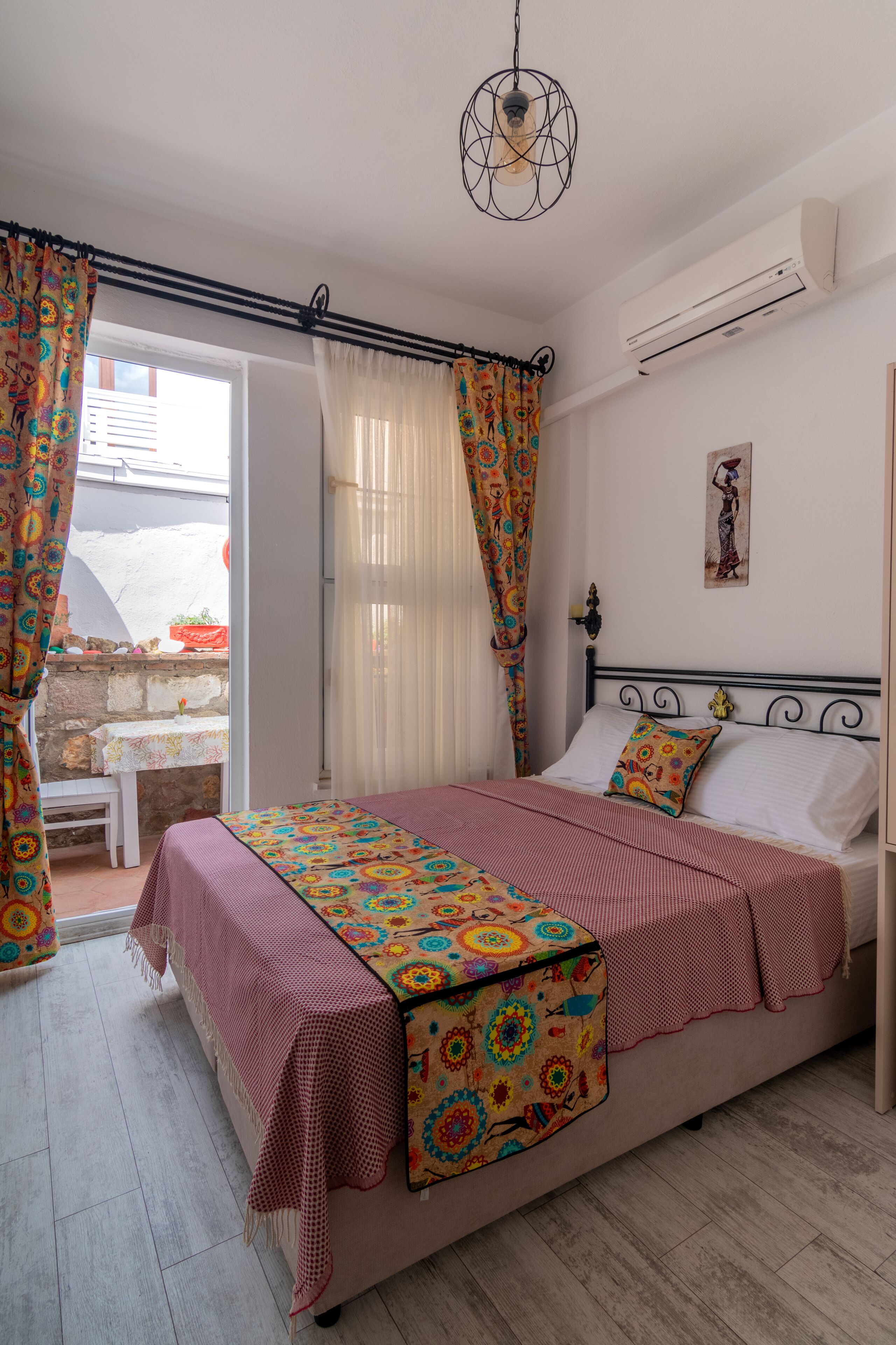 A bedroom with a bed, a bedside table, a hanging light fixture, and a window with curtains.