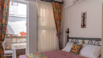 A bedroom with a bed, a bedside table, a hanging light fixture, and a window with curtains.