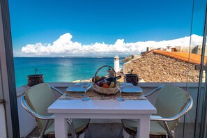 Una mesa dispuesta con frutero y copas de vino, con vistas a la costa, una pared de piedra y un faro.