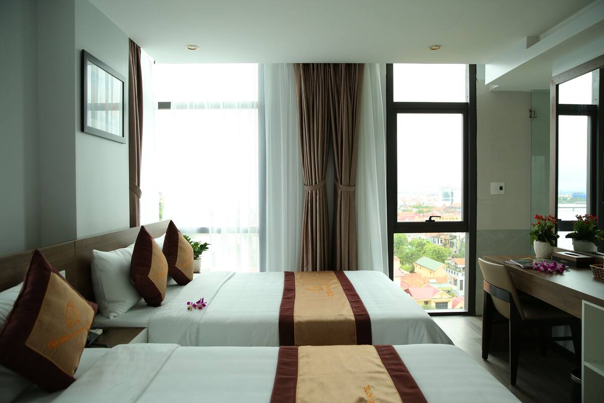 Une chambre d’hôtel avec deux lits, un bureau et une grande fenêtre donnant sur la ville.