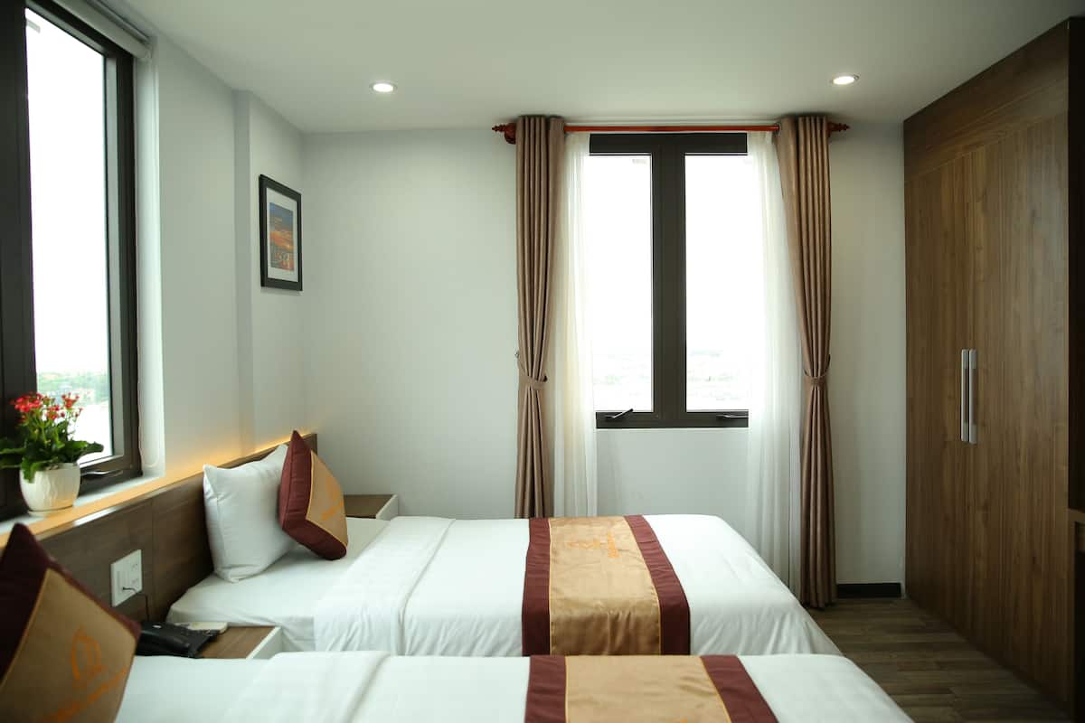 Une chambre d’hôtel avec deux lits, une armoire en bois, une fenêtre avec des rideaux et une plante en pot sur le rebord de la fenêtre.