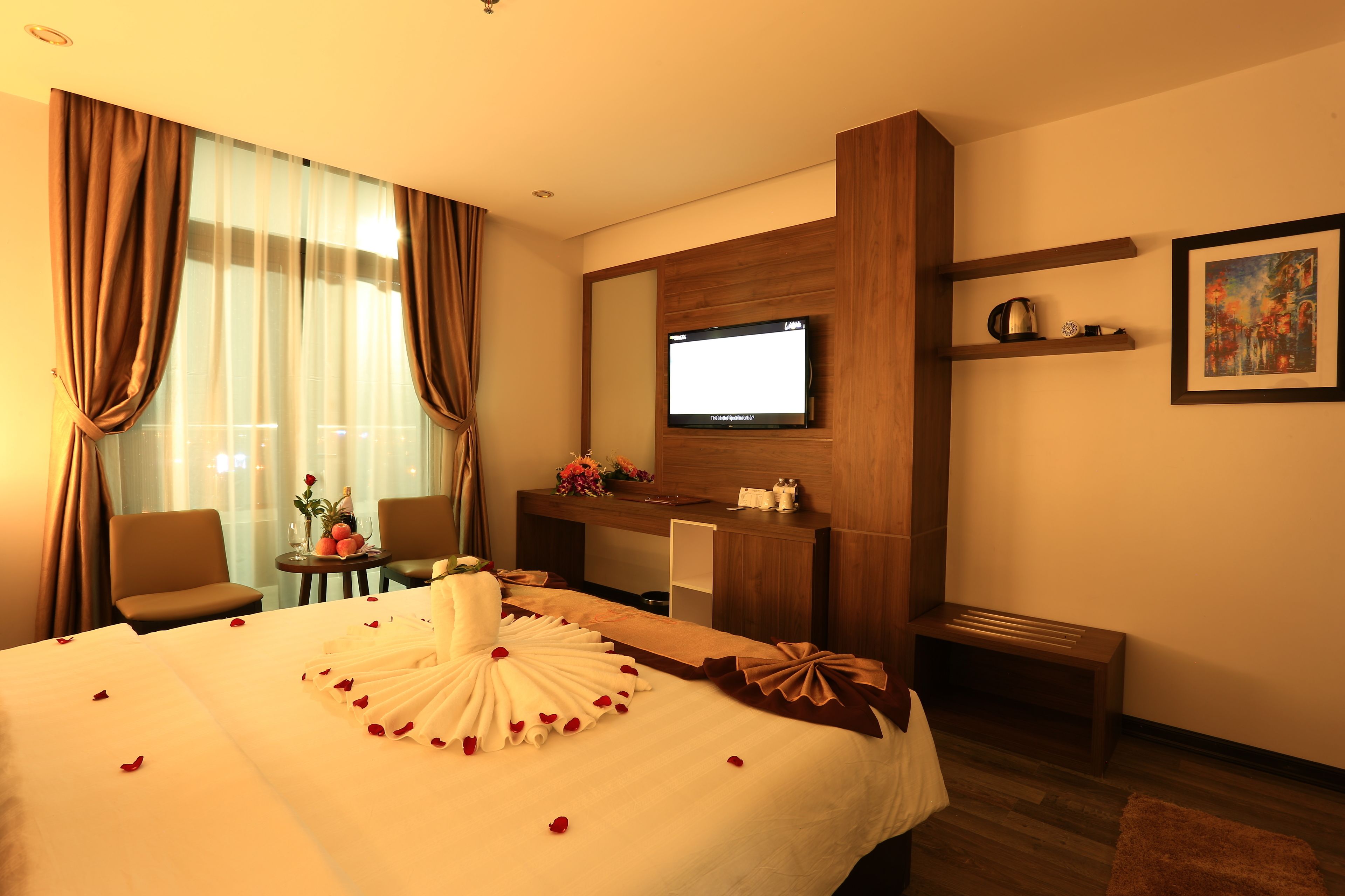 A hotel room with a bed, a desk, a television, and a painting on the wall.