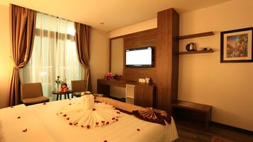 A hotel room with a bed, a desk, a television, and a painting on the wall.