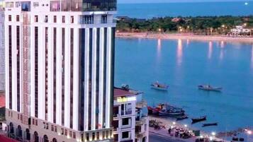 A tall hotel with a modern design, located near a waterfront with boats visible in the water.