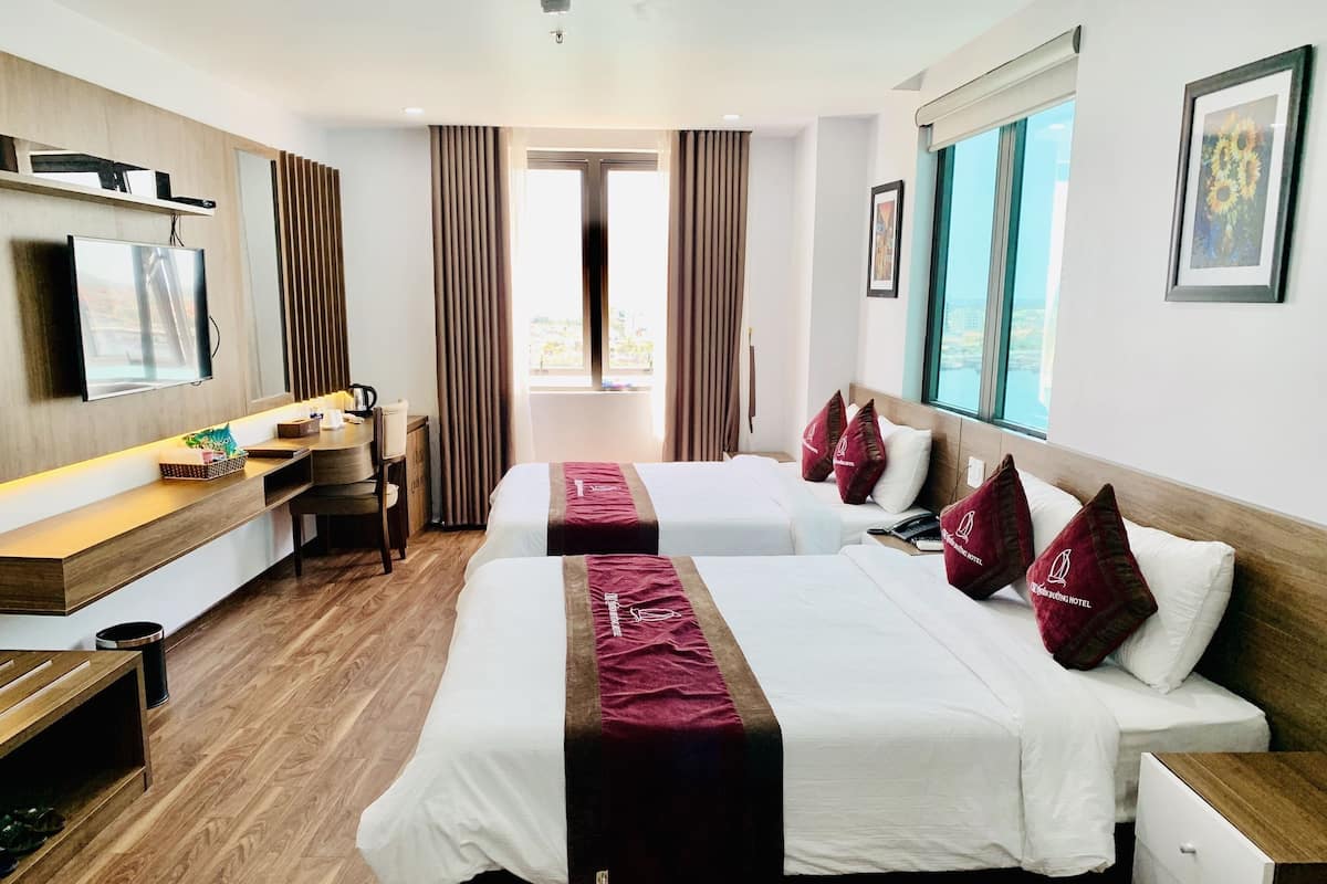 Une chambre d’hôtel avec deux lits, un bureau, une télévision et une fenêtre donnant sur un paysage agréable.