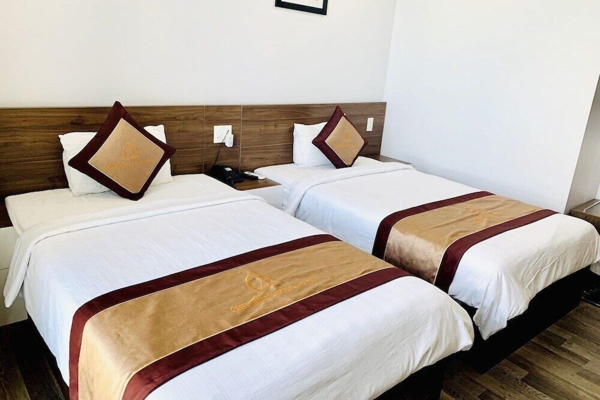 Une chambre d’hôtel avec deux lits, chacun agrémenté de draps blancs et d’oreillers décoratifs marron.