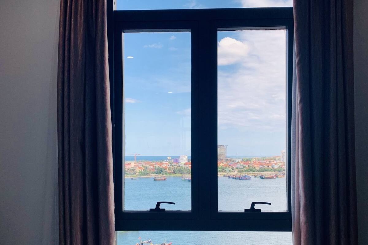 Une chambre d’hôtel dotée d’une grande fenêtre donnant sur un plan d’eau et sur le paysage urbain.