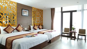 A hotel room with two beds, a sitting area with chairs, a decorative wall panel, and a large window.