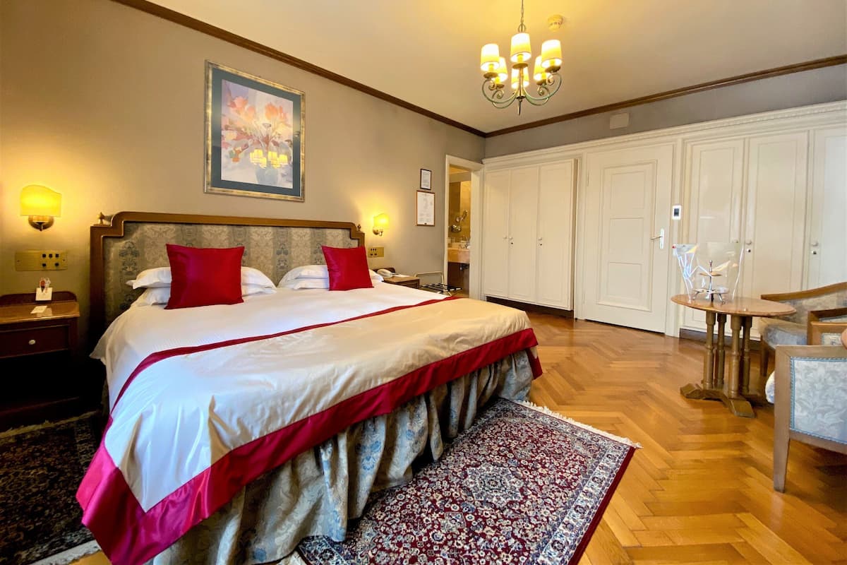 Ein geräumiges Schlafzimmer mit einem großen Bett, einer Chandelüster, einem Kleiderschrank und einem kleinen Tisch mit Stühlen.