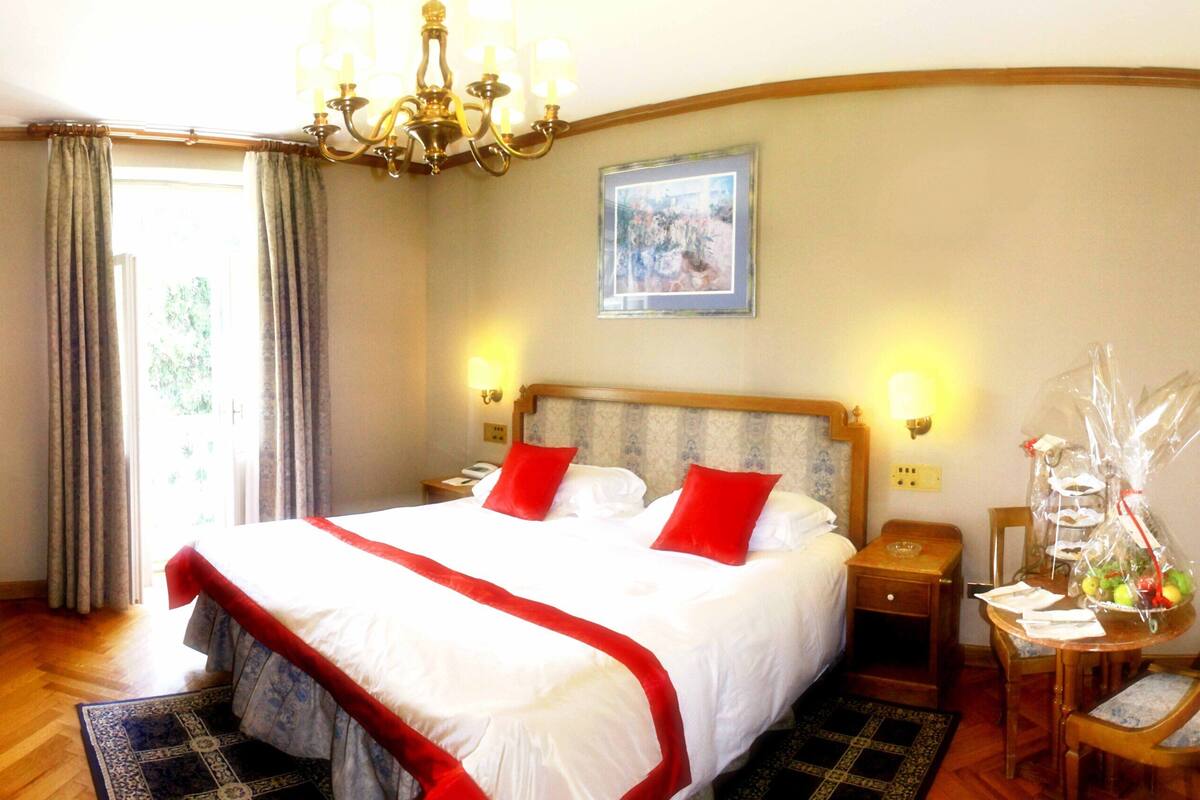 Ein Hotelzimmer mit einem großen Bett, einer Chandelüster, einem Esstisch mit Stühlen und einer Blumenvase.